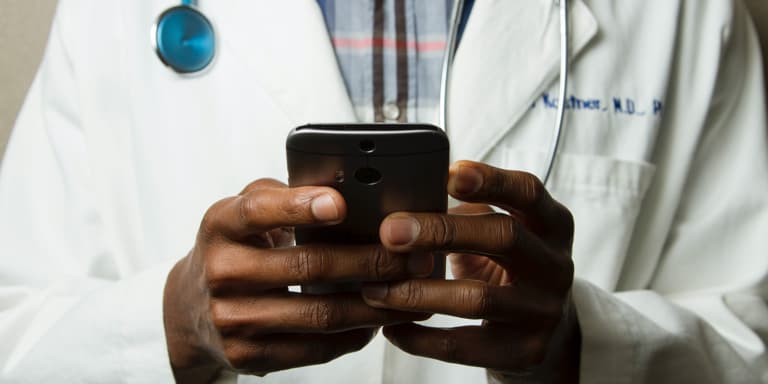 A doctor with his stethoscope around his neck, using his cell phone.