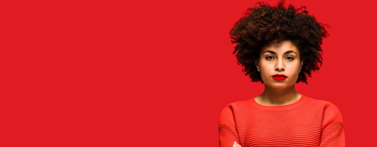 A woman in a red cardigan stands with her arms folded as she proudly owns her success.