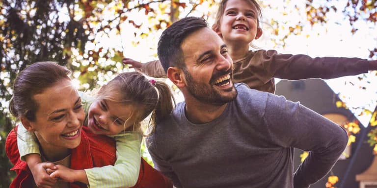 Mom and Dad joyously laughing with their two young daughters while giving them piggyback rides.