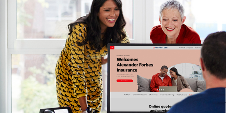 Two ladies look at their colleague who is sitting in front of his computer with approving smiles upon hearing about the acquisition of Alexander Forbes Insurance (AFI) under the Momentum brand. AFI is now known as Momentum Insurance (MI).