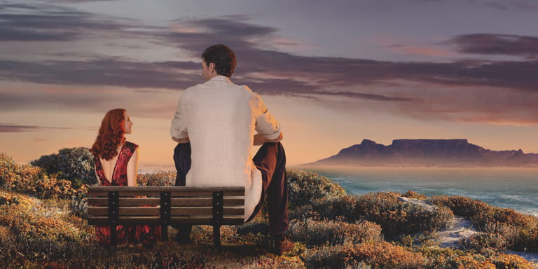 Alice and Matt sitting on a bench with the sea and Table Mountain in front of them.