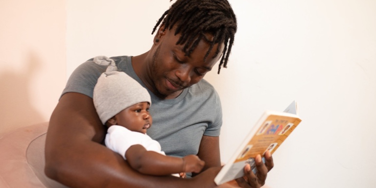 A father holding his baby as they read a story book.