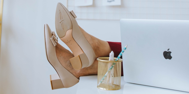 A woman’s feet placed on the table next to a laptop and a pencil container 