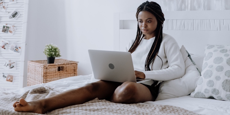 A lady sitting on a bed submitting her tax returns on her laptop. 