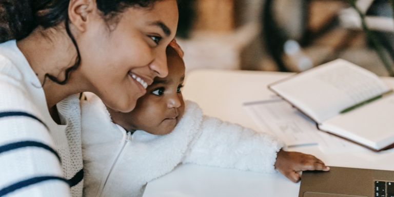 A mother and her baby looking at a laptop screen and smiling.