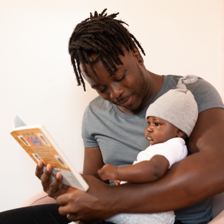A father holding his baby as they read a story book.