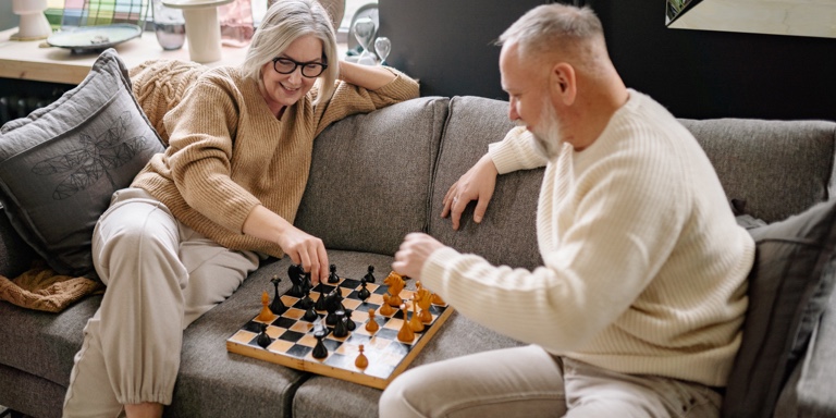 An old couple enjoying their retirement while sitting at a couch playing a game of chess.