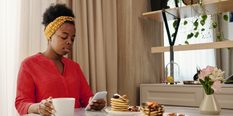 A lady having coffee and pancakes while scrolling on her cellphone.  