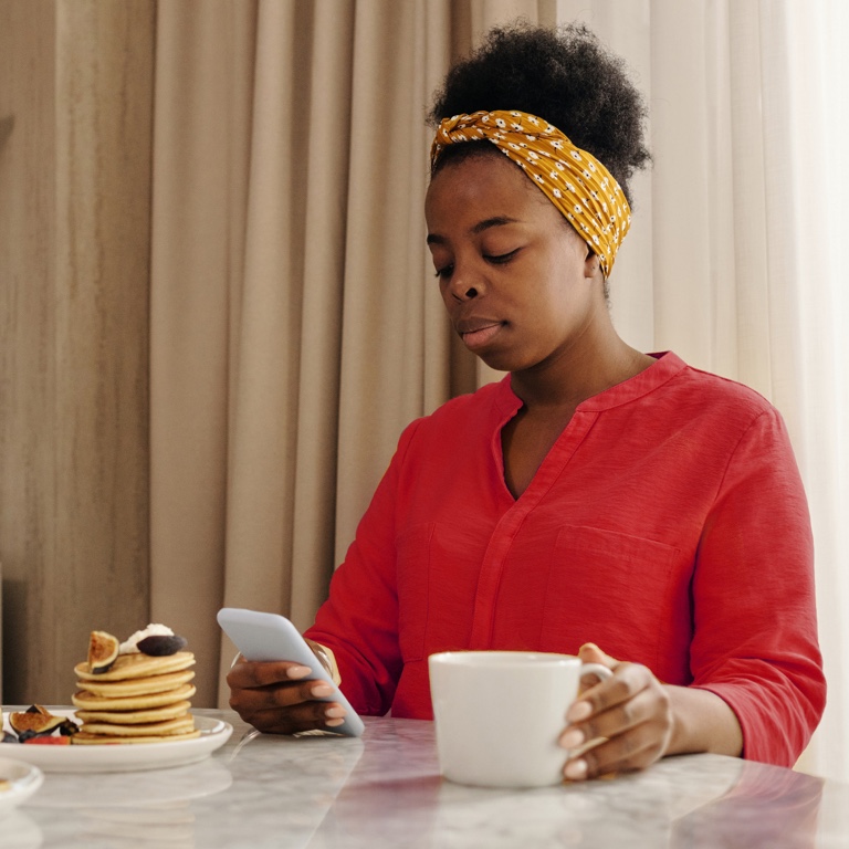 A lady having coffee and pancakes while scrolling on her cellphone.