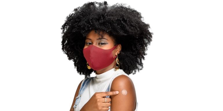 A vibrant young lady wearing a mask and a sleeveless t-shirt pointing to her upper where she received the COVID-19 vaccine, doing her part to achieve population immunity.