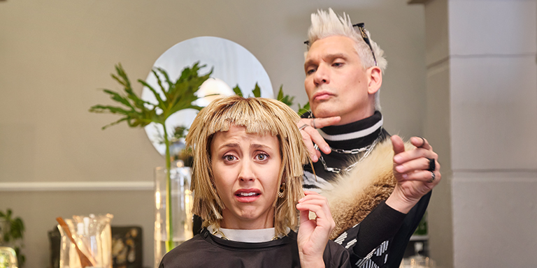 A young lady looks horrified at her new hairstyle while her trendy hairstylist looks on quite pleased with the outcome.