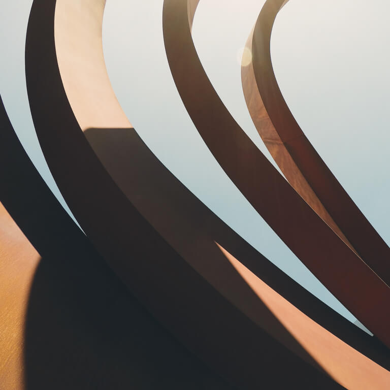 A looking up into the sky through the inside of a modern abract building with curved rustic steel spirals at the top.