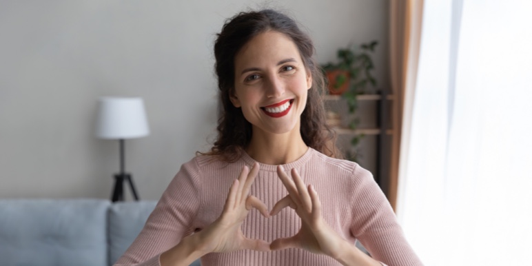 A young woman smiling and creating a heart shape with her hands.