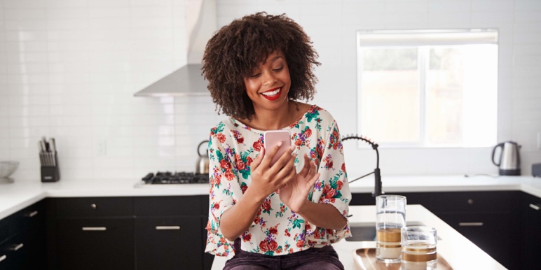 A young woman smiles as she looks at her cell phone.