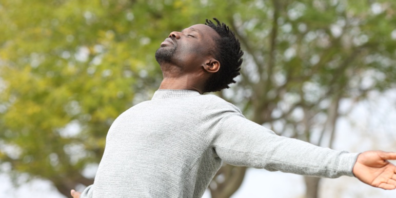 A young African man closes his eyes and stretches his arms out in a park