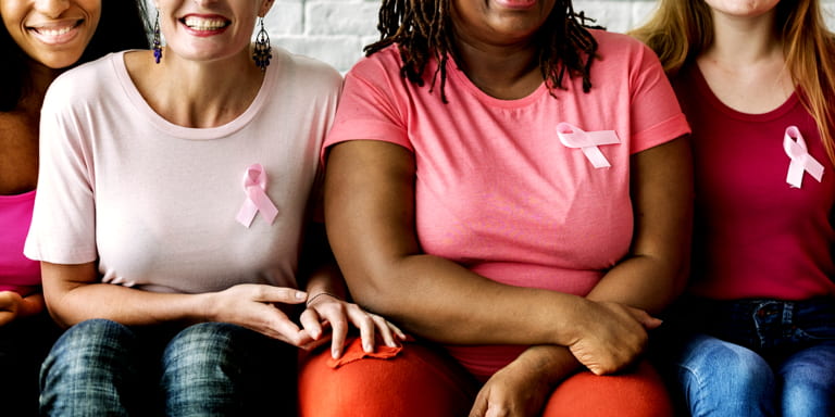 4 young ladies seated in a row wearing pink t-shirts with pink ribbons on.