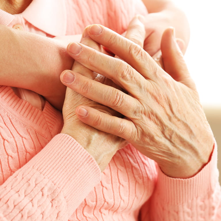 Close up picture of an elderly womans hands where one hand is placed over the other.