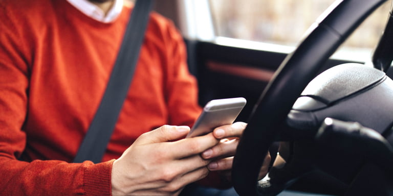 A man in the driver's seat in his car, accessing Momentum  Insure's Safety Alert on his phone in a step-by-step video of how it works.