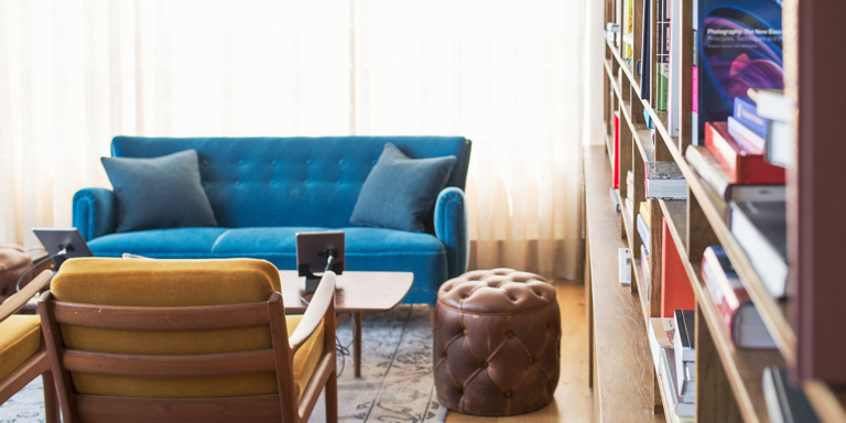 Achieve the home you’ve dreamt of so you can have that comfortable living area to relax in. Pictured here is a blue couch, ottoman and bookshelf filled with books.