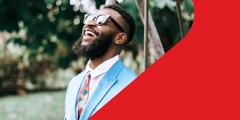 Successful, bearded young man in a pale blue suit and hexagonal patterned tie wearing sunglasses as he optimistically looks up towards the sky.