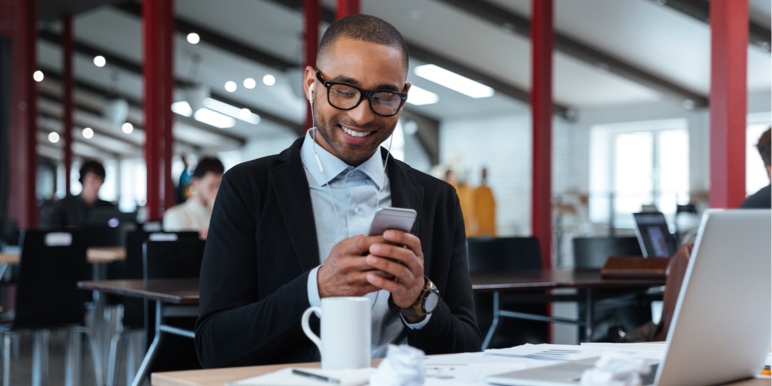 Busy man working on his phone at a desk full of papers with a coffee mug.