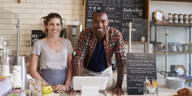 A white woman and a Black man are standing behind a counter at a coffee shop