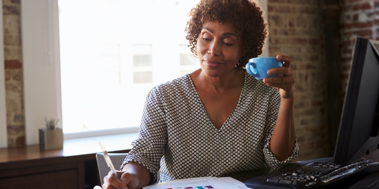 A Black woman working happily holding her coffee mug