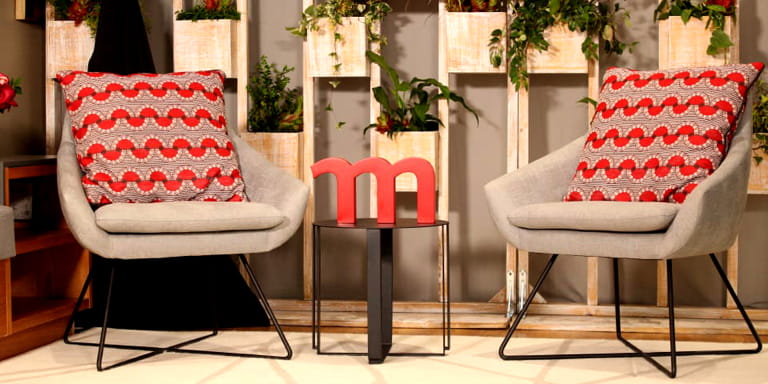 Two grey chairs with vibrant red and grey cushions on them.