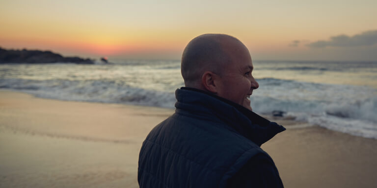 Side view of a man standing on the sea shoreline looking out towards the sea.