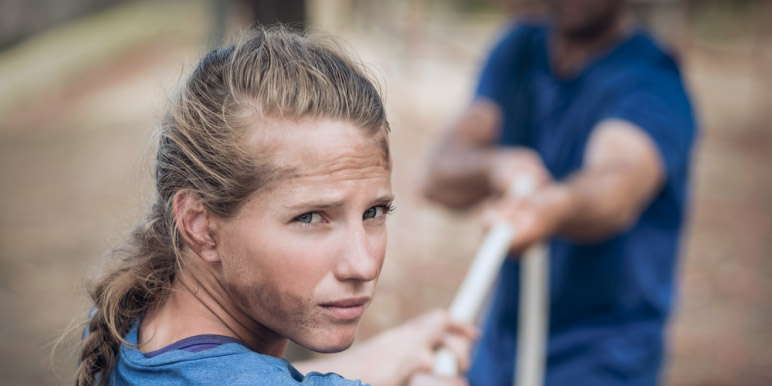 A young female looking at the camera while she pulls on a rope that is held on the other end by a male.