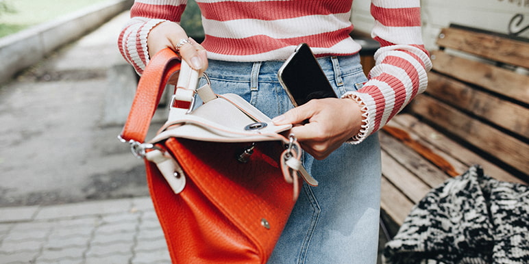 A young female opening her bag to place her cell phone inside. Momentum Insure ha a specific cover for females that covers handbag loss or theft and its contents.