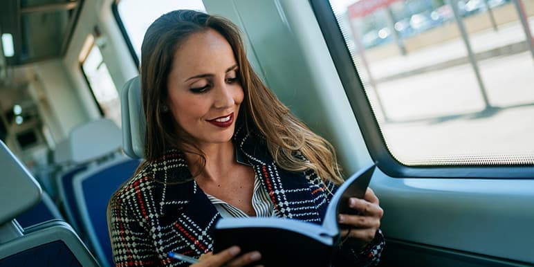 A woman sitting on a train heading safely to her next destination, earning herself a Safe Day, while reading her planner to prepare her for the rest of the day.