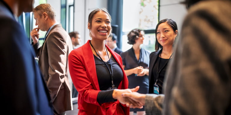 A young female employee shaking hands with another employee at a member conference.