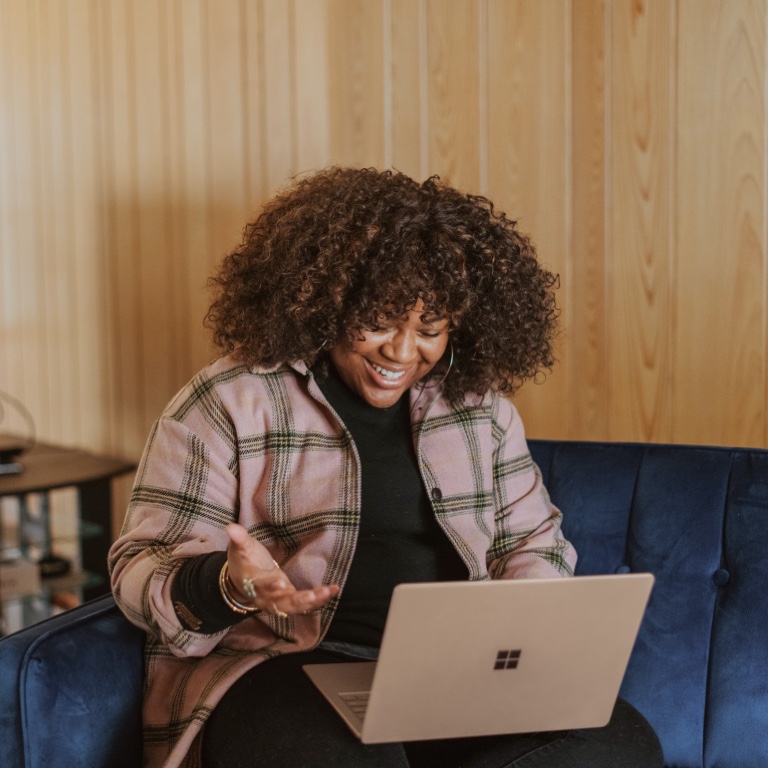 A young woman sitting on a blue velvet couch using the Smart Solutions tool on her laptop to view her benefits and profile.