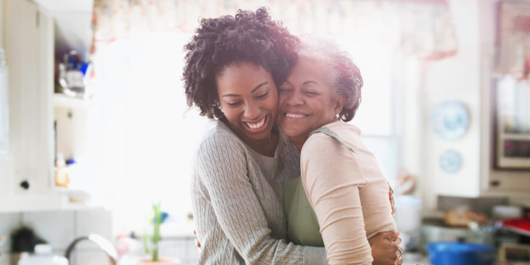 A mom hugs her young smiling  daughter with eyes closed. They both are wearing yellow tops and have dark long hair.  