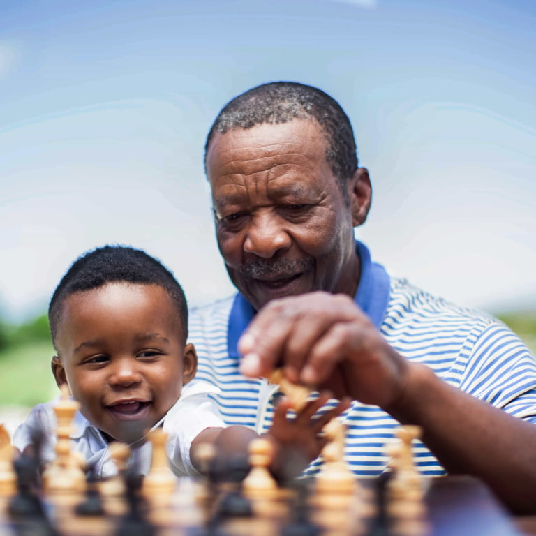 An old man enjoys retirement playing chess with his toddler grandson.