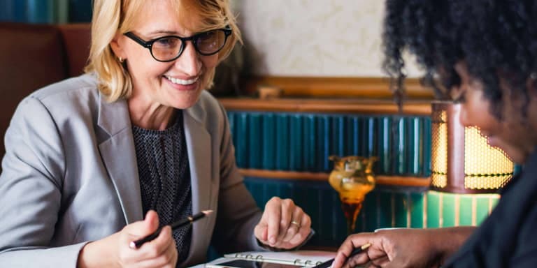 Two women sitting at a table having a pleasent conversation with FundsAtwork documents on the table.