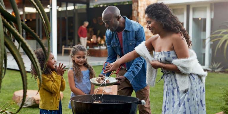 A young couple making a braai/barbeque with their two young daughters in their beautiful back yard.