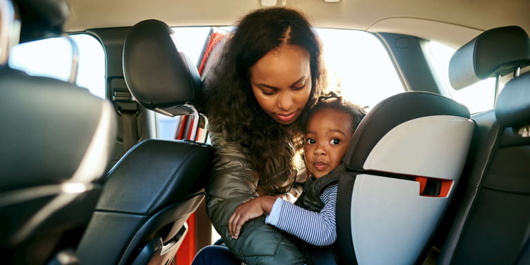 A young mom strapping in her daughter into her car seat behind the driver's seat.