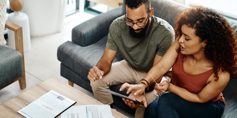 A man and woman sitting on a black couch, working through their financial documents.