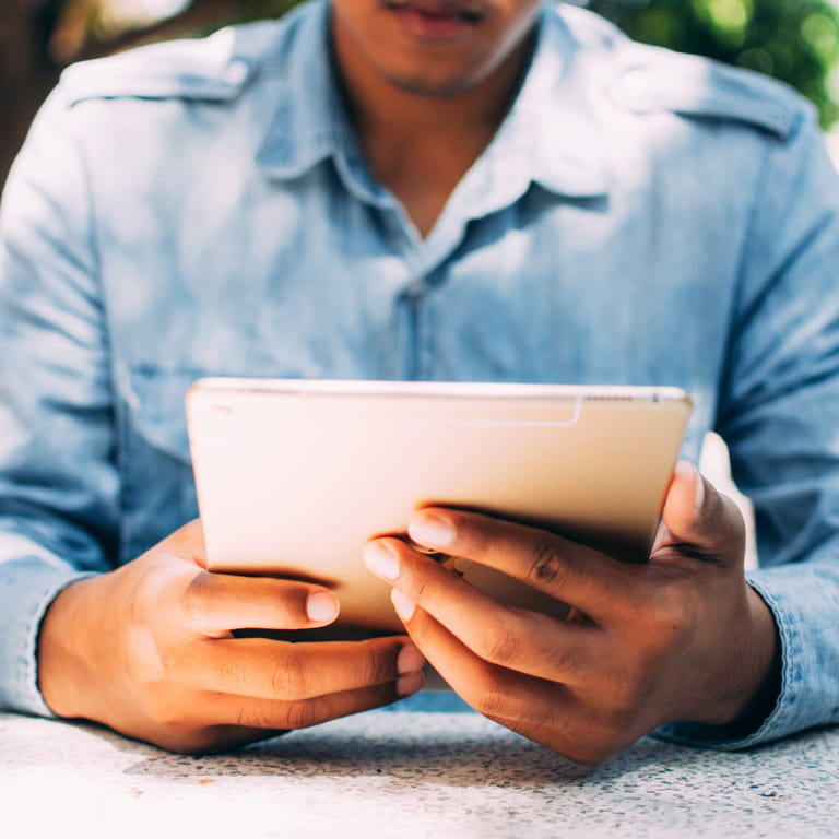 A woman in a light blue shirt holding, and working on her tablet.