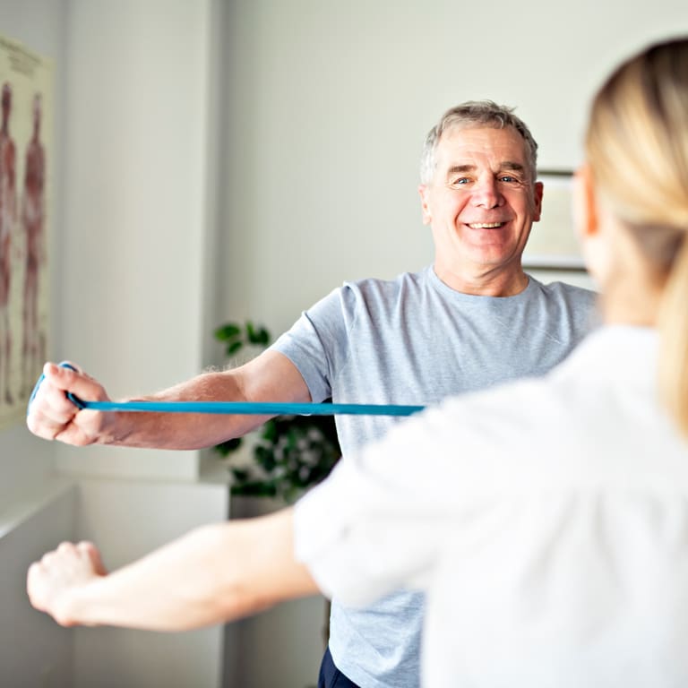 An older male using a resistance band for resistance training whilst training with his female personal trainer.