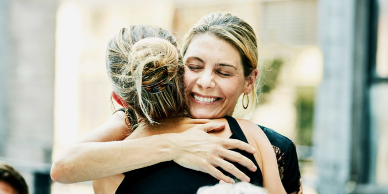 Two women in town are happy to see each other, they are smiling and hugging each other tightly.