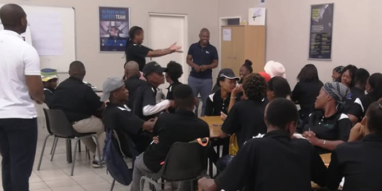A classroom packed with youth dressed in black talking amongst each other.