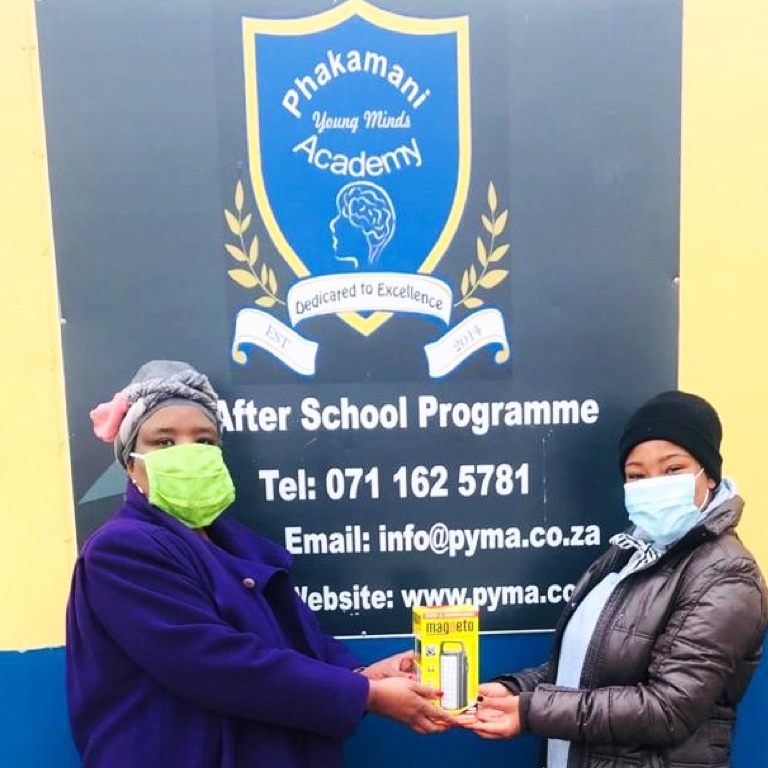 Two women with masks handing over a gift in front of a school.