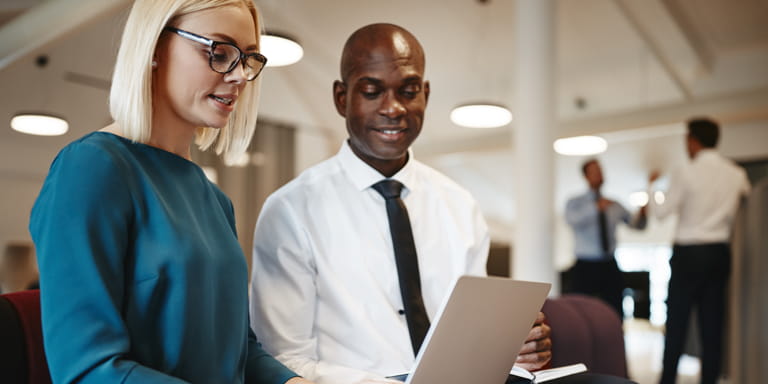 Two financial advisors, male and female, reviewing some financial planning documents on an open laptop in front of them.  