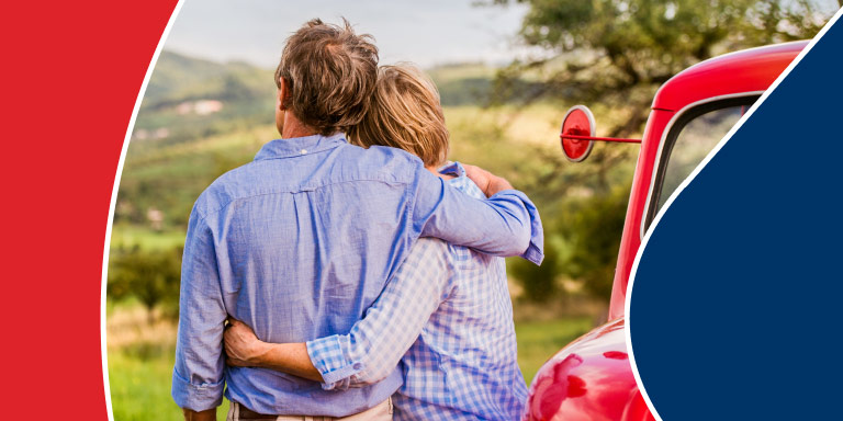 A couple leaning against their red vintage truck looking at the beautiful rolling hills view in front of them, happy that they sought the advice of a financial adviser to keep them on track with their retirement goals.