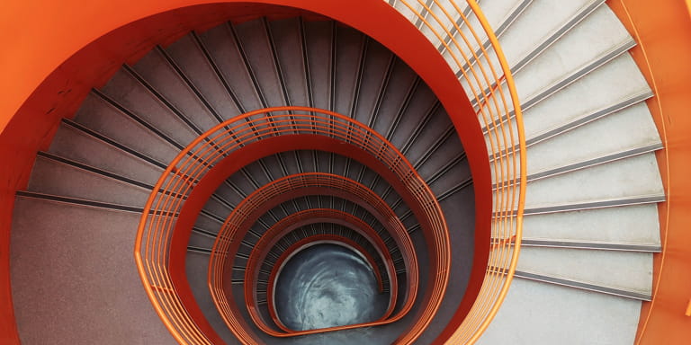 Spiral staircase with vibrant orange walls and washed grey stairs from a birds eye view.