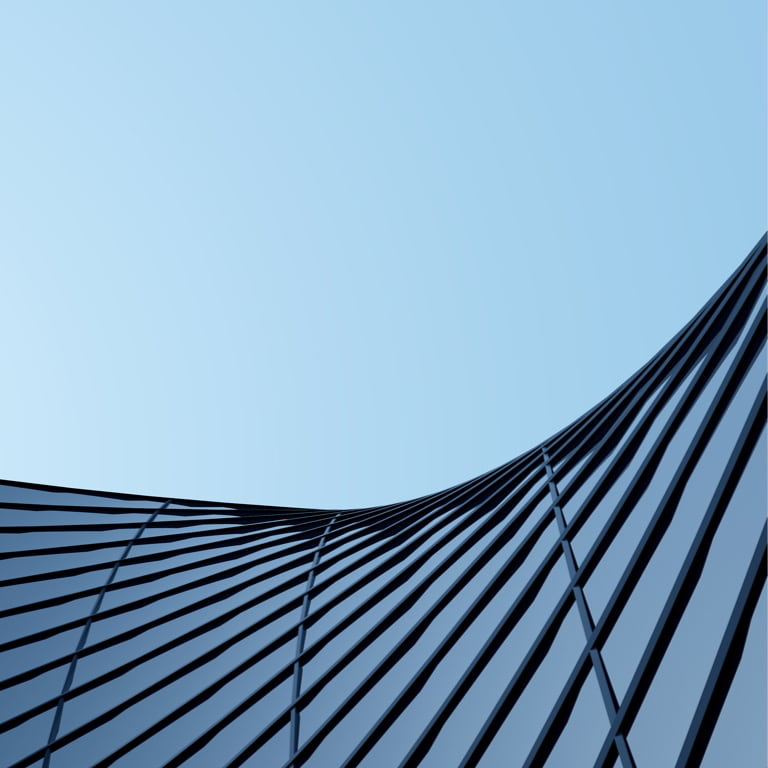 Curved, glass and steel exterior wall of modern high-rise office building against a blue sky backdrop.