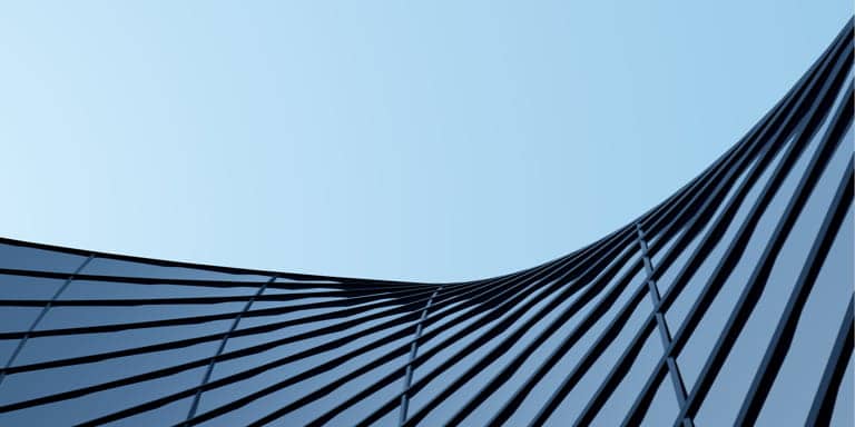 Curved, glass and steel exterior wall of modern high-rise office building against a blue sky backdrop.